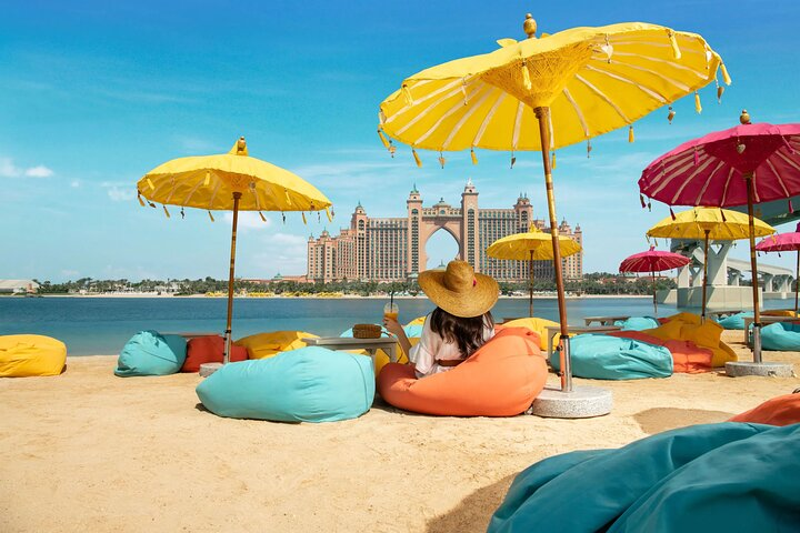 Relax on the sandy shores under colorful umbrellas gazing at the iconic Atlantis Palm while enjoying the serene beauty and unique charm of Dubai's coastline.